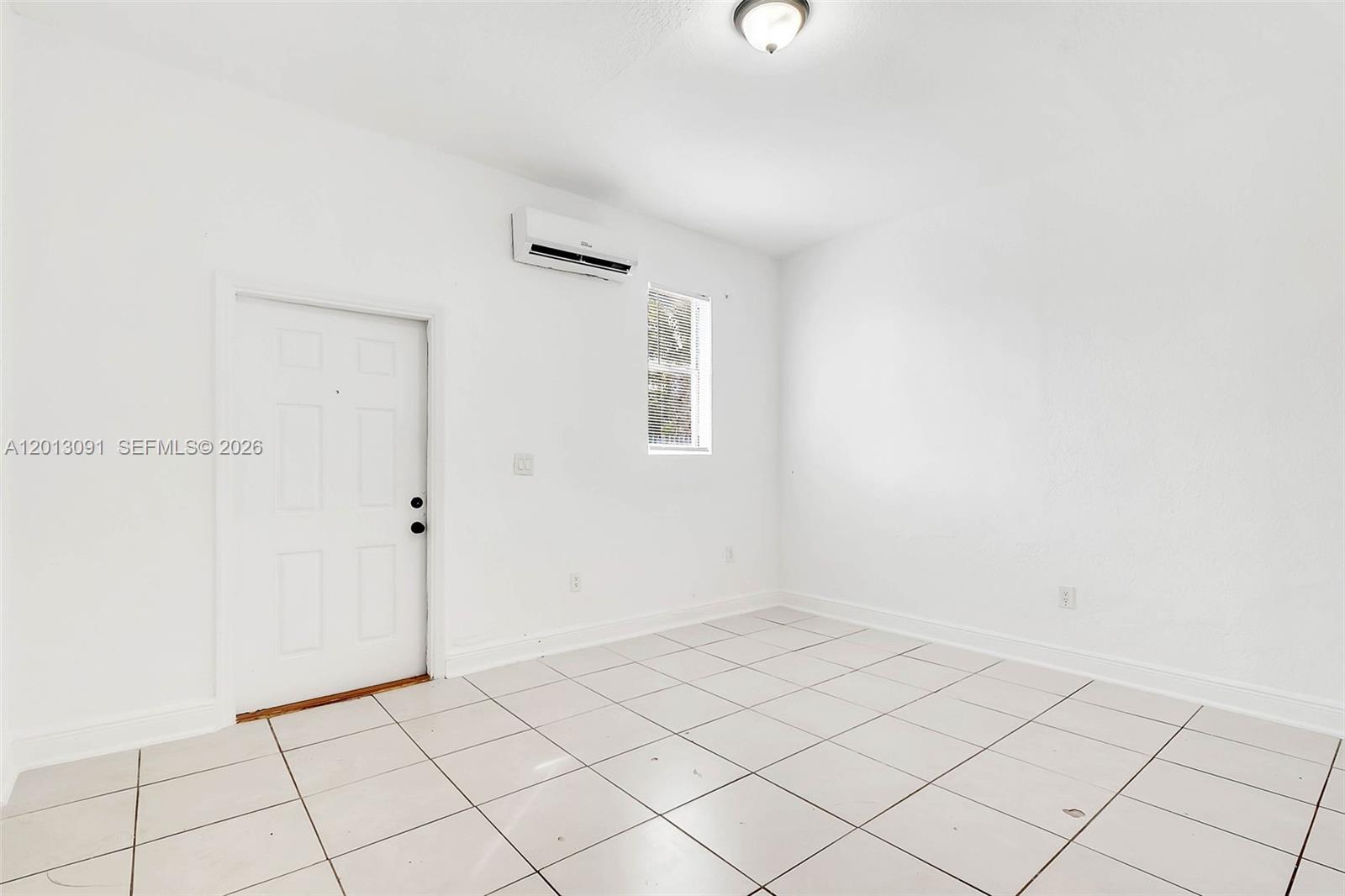 A small, empty room features white walls, tiled flooring, a white door, and a wall-mounted AC — 50 NW 79th St # 4, Miami FL 33150, MIAMI, FL