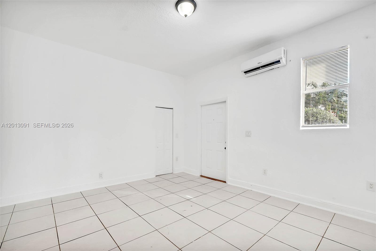 A bright, empty room features white walls, light-colored tile flooring, a window, and a wall-mounted air conditioner — 50 NW 79th St # 4, Miami FL 33150, MIAMI, FL