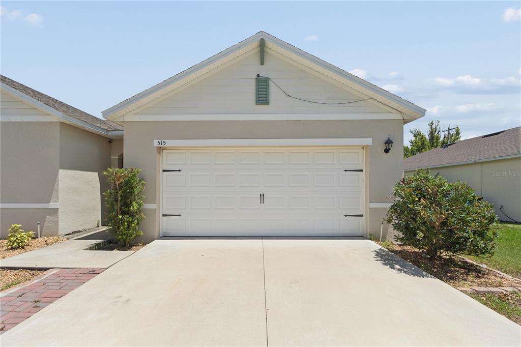 A single-story house exterior features a white garage door, beige siding, and a concrete driveway — 515 AUBURN GROVE TERRACE, AUBURNDALE, FL