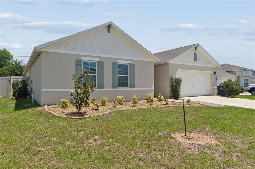 A single-story house with a beige stucco exterior, blue shutters, and an attached two-car garage — 515 AUBURN GROVE TERRACE, AUBURNDALE, FL