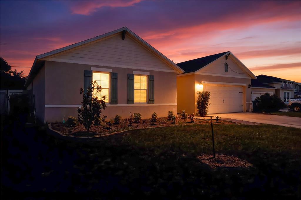 A single-story house with a two-car garage and landscaped front yard at sunset — 515 AUBURN GROVE TERRACE, AUBURNDALE, FL