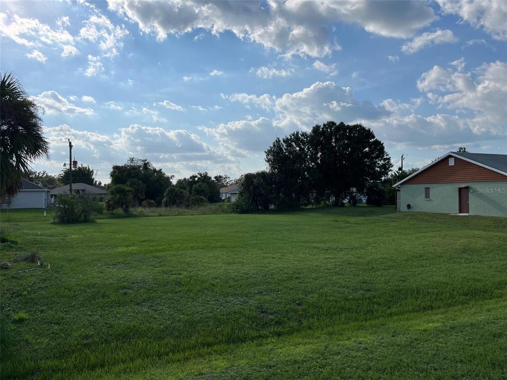 A large, grassy vacant lot sits between a residential house and a line of trees — 2361 S BISCAYNE DRIVE, NORTH PORT, FL