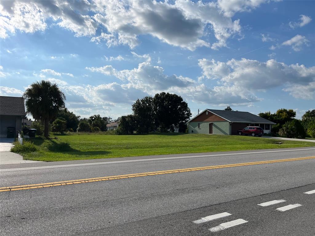 A vacant grassy lot sits between two houses along a paved road under a cloudy sky — 2361 S BISCAYNE DRIVE, NORTH PORT, FL