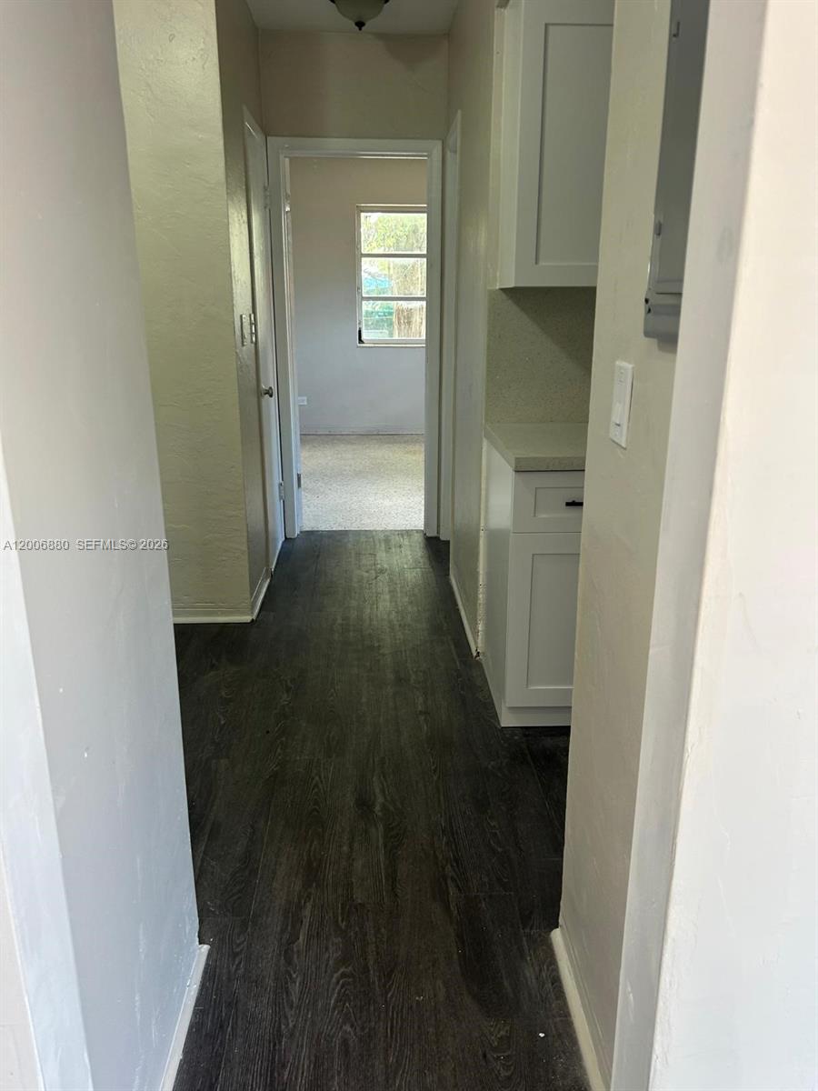 A hallway with dark wood-look flooring leads to a doorway showing a room with windows — 1743 NW 15th St # 1743, Miami FL 33125, MIAMI, FL