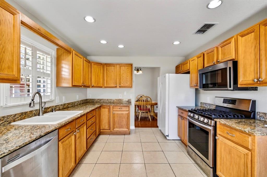 A kitchen with wood cabinets, granite countertops, stainless steel appliances, and tile flooring — 35653 CALLA COURT, LEESBURG, FL