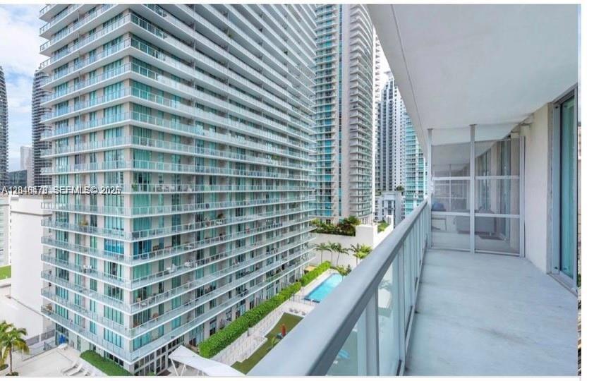 A balcony with a glass railing overlooks a swimming pool and neighboring high-rise apartment buildings — 79 SW 12th St, Miami FL 33130, MIAMI, FL