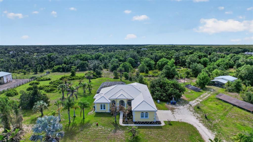 An aerial view shows a yellow house with a white roof surrounded by green trees — 1210 408TH COURT E, MYAKKA CITY, FL
