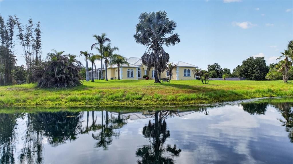 A yellow house sits behind a pond surrounded by palm trees and grassy landscaping — 1210 408TH COURT E, MYAKKA CITY, FL