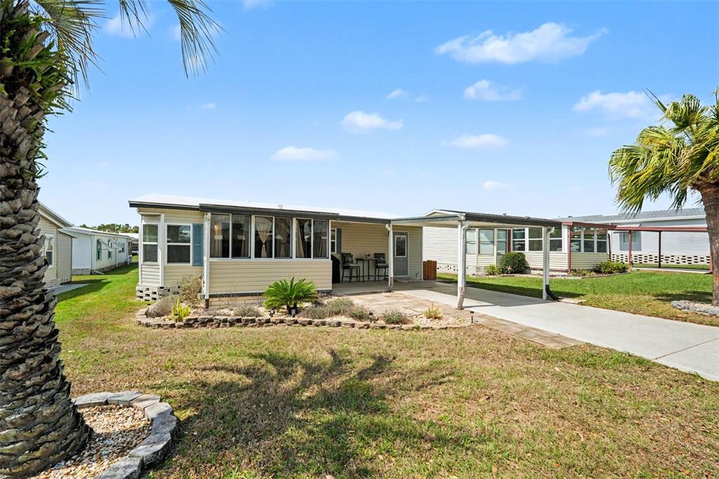 A single-story manufactured home with a carport, concrete patio, and palm trees in the yard — 7123 SIESTA STREET, ZEPHYRHILLS, FL