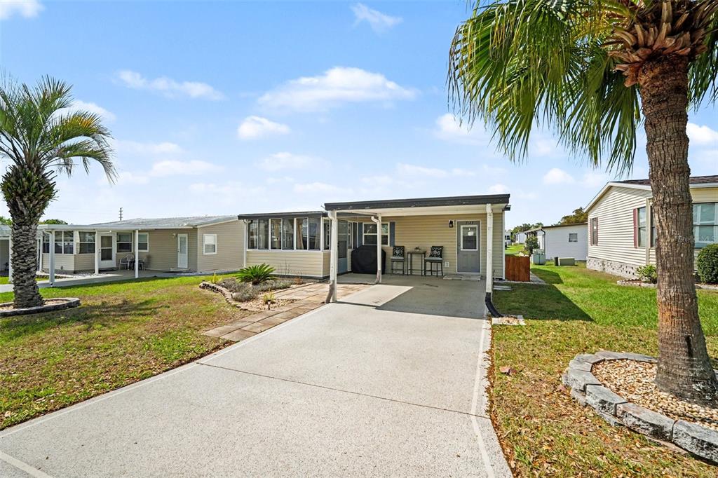 A single-story manufactured home features a concrete driveway, a covered carport, and two palm trees — 7123 SIESTA STREET, ZEPHYRHILLS, FL