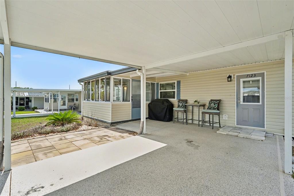 A covered carport area features a concrete floor, a small patio set, and an entrance — 7123 SIESTA STREET, ZEPHYRHILLS, FL
