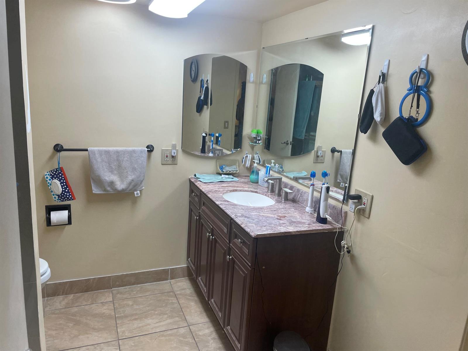 A bathroom features a dark wood vanity with a marble countertop, a mirror, and tile flooring — 1101 NW 58th Terrace # 404, Sunrise FL 33313, SUNRISE, FL