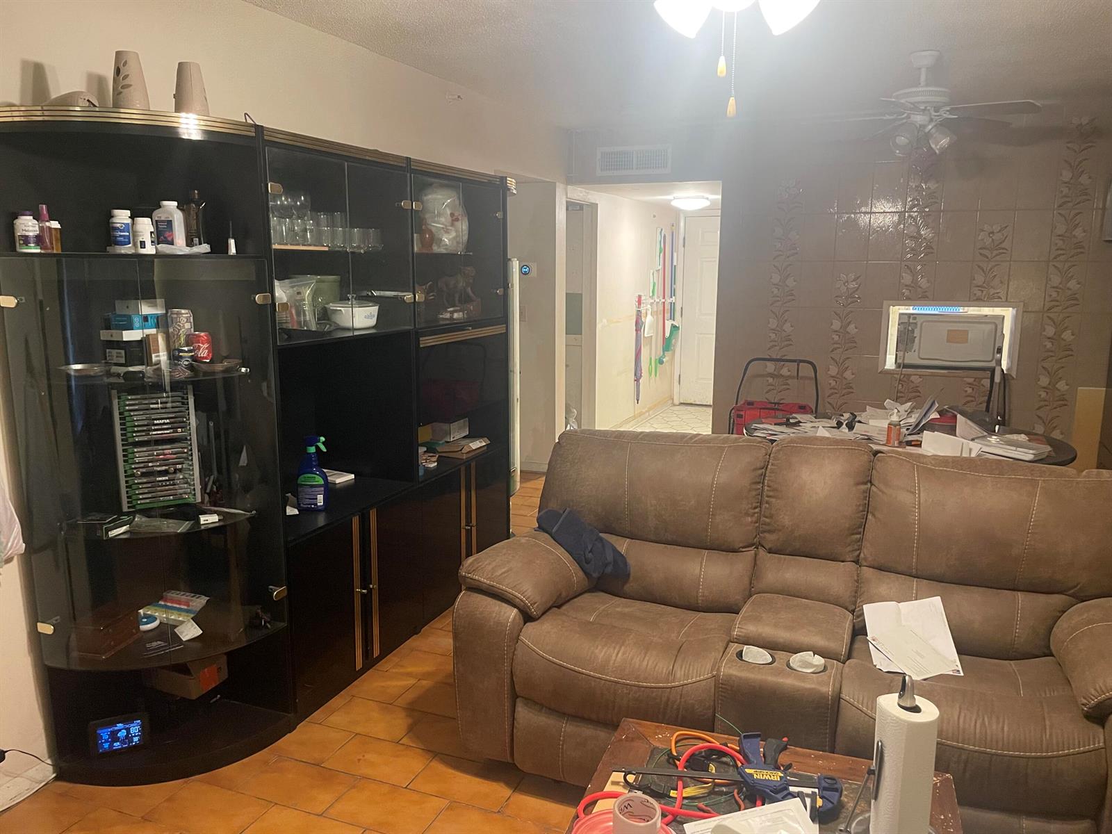 A living room features a large black display cabinet, a brown reclining sofa, and tiled flooring — 1101 NW 58th Terrace # 404, Sunrise FL 33313, SUNRISE, FL