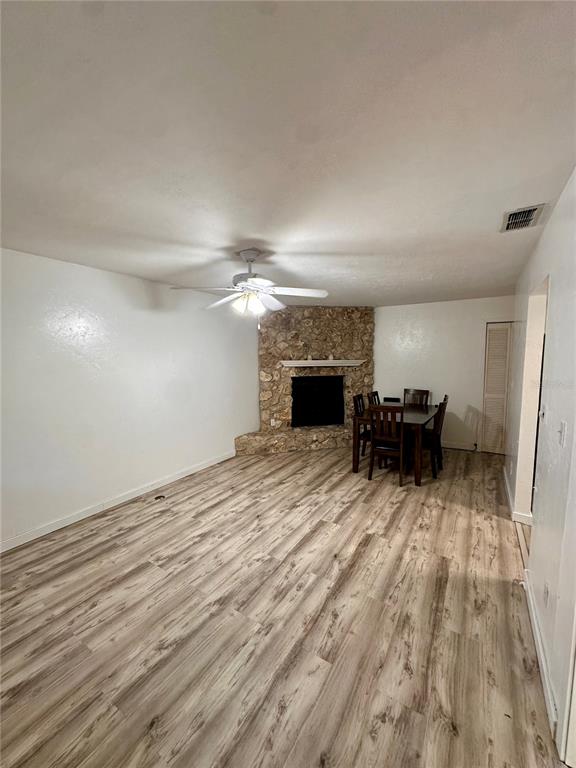 A room with wood-look flooring, a ceiling fan, and a corner stone fireplace — 223 NW 34TH STREET, GAINESVILLE, FL