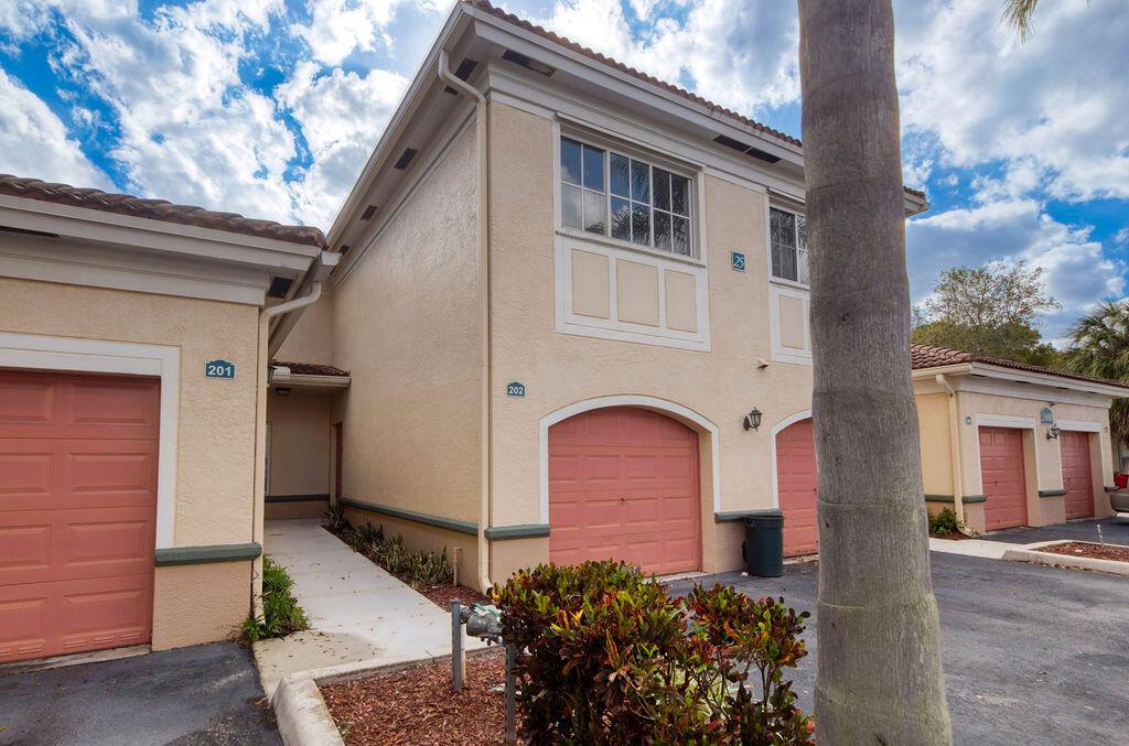 The exterior of a multi-unit residential building features tan stucco walls and pink garage doors — 2400 Centergate Dr # 202, Miramar FL 33025, MIRAMAR, FL