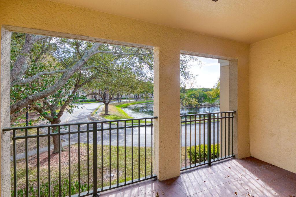 A covered balcony with tile flooring and a metal railing overlooks a pond and trees — 2400 Centergate Dr # 202, Miramar FL 33025, MIRAMAR, FL