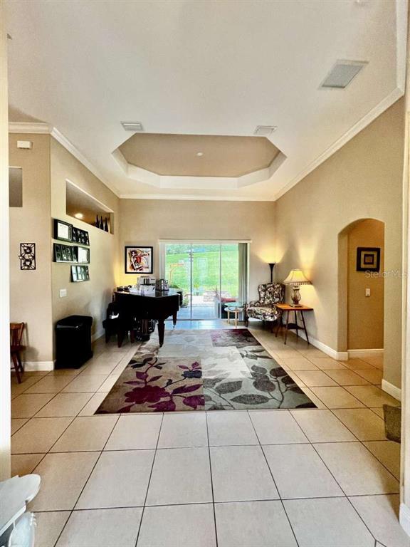 A living room features a tray ceiling, tile flooring, a grand piano, and sliding glass doors — 16325 MAGNOLIA BLUFF DRIVE, MONTVERDE, FL