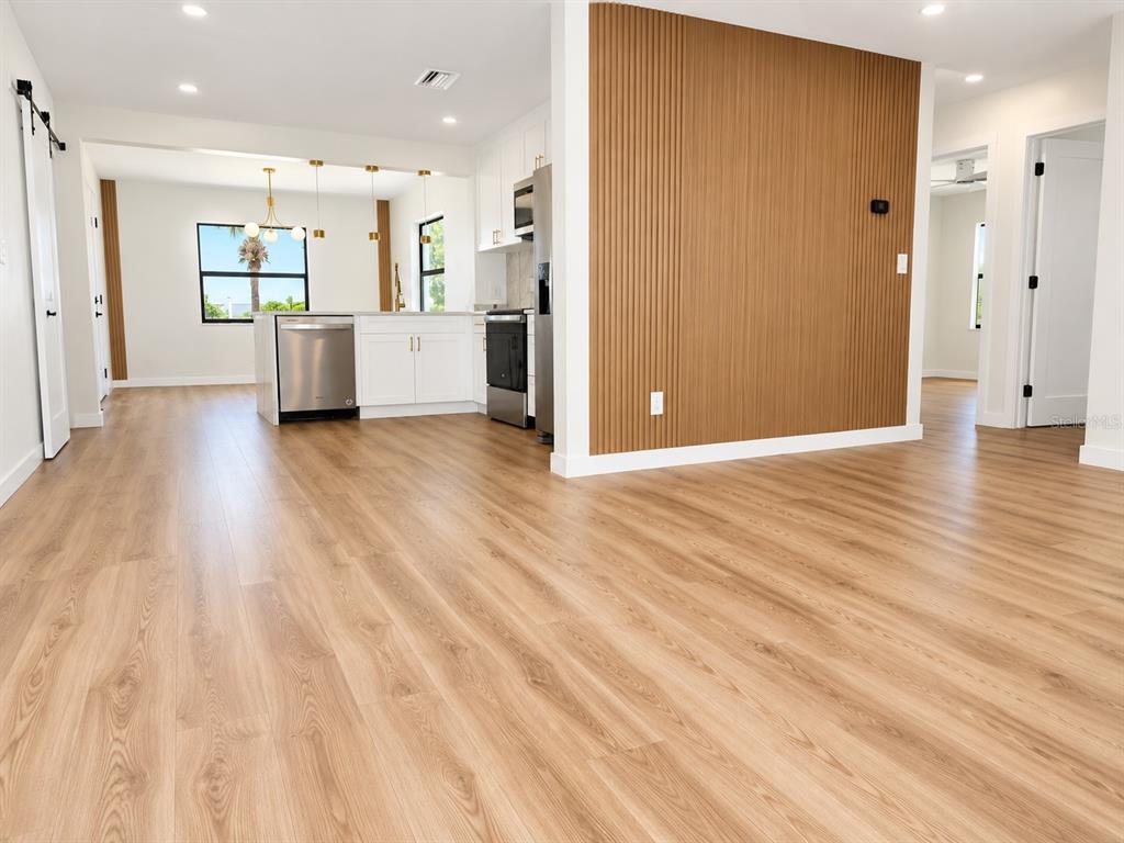 A kitchen with white cabinets and stainless steel appliances sits beside a wood-slatted accent wall — 8120 7TH STREET N, ST PETERSBURG, FL