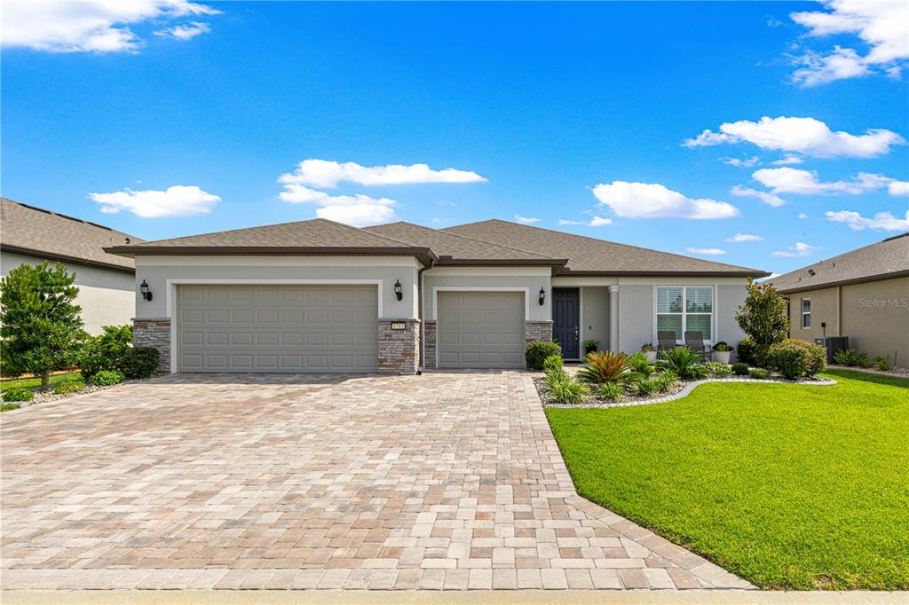 A single-story house features a paver driveway, a three-car garage, and a landscaped front lawn — 8783 SW 57TH PLACE ROAD, OCALA, FL