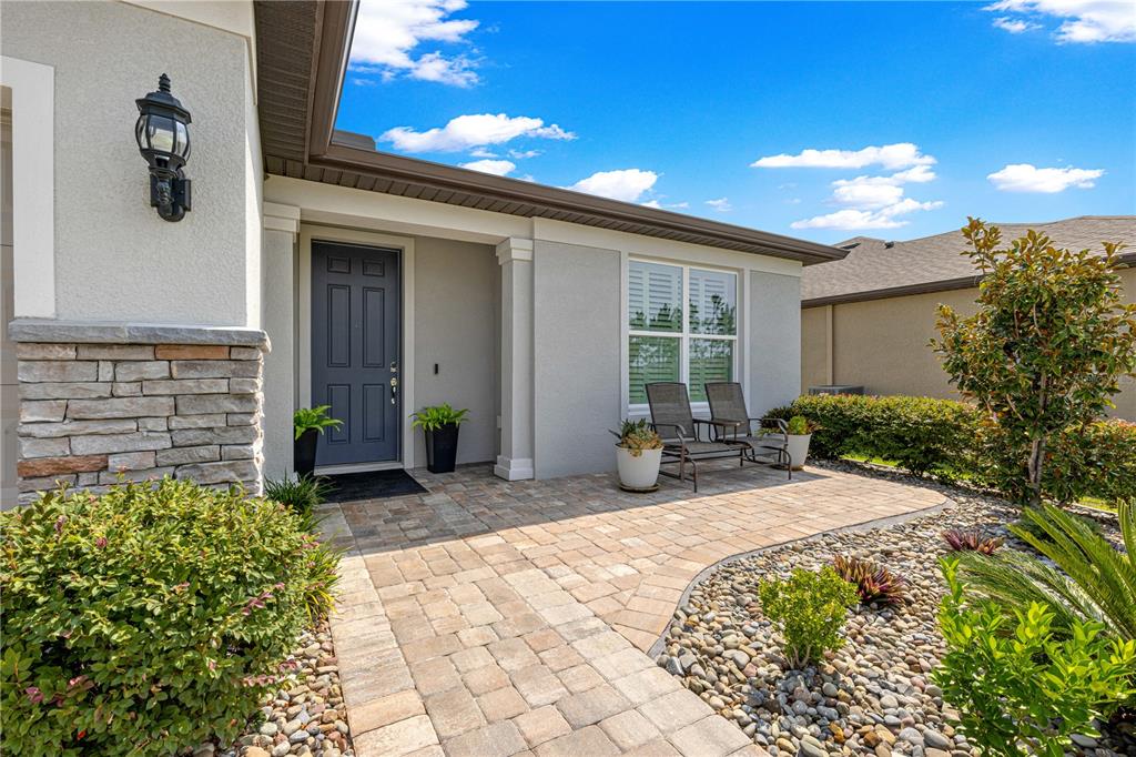 A paved walkway leads to the front entrance of a house with stone accents — 8783 SW 57TH PLACE ROAD, OCALA, FL