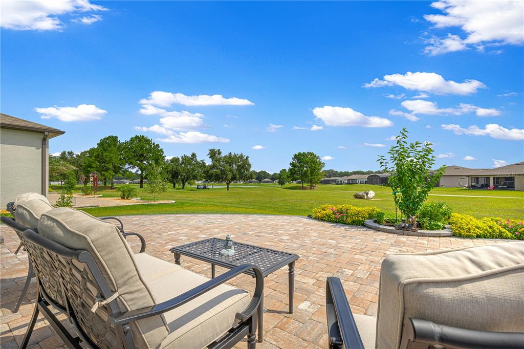 A paved patio with outdoor furniture overlooks a grassy lawn and distant trees — 8783 SW 57TH PLACE ROAD, OCALA, FL