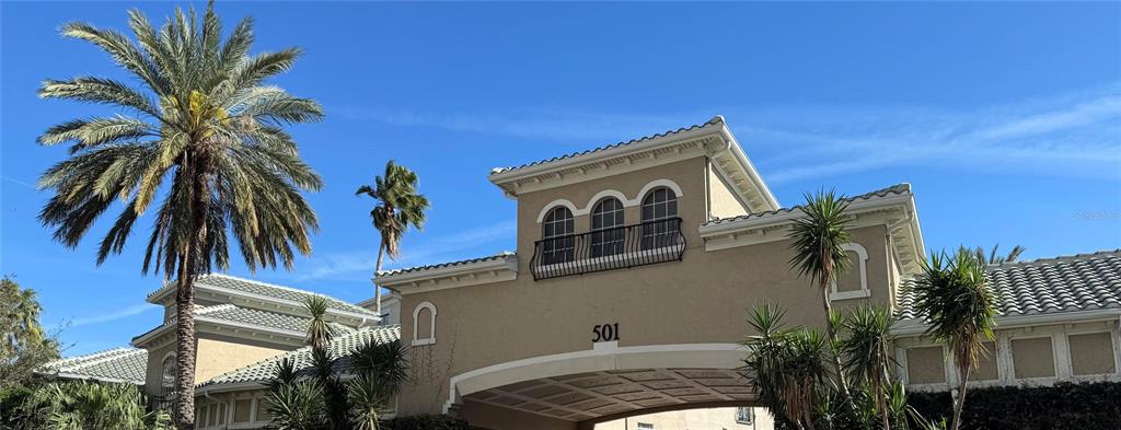 A tan building exterior features a central arched entryway and a balcony with black railings — 501 KNIGHTS RUN AVENUE UNIT 2106, TAMPA, FL