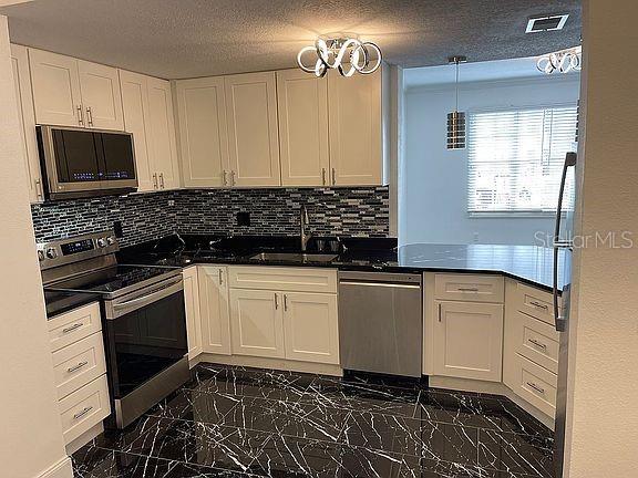 A kitchen with white cabinets, black countertops, a tiled backsplash, and black marble-patterned flooring — 501 KNIGHTS RUN AVENUE UNIT 2106, TAMPA, FL