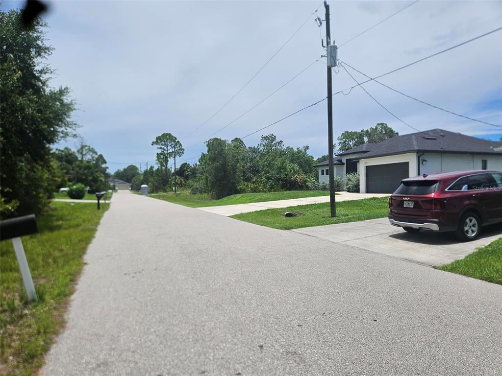 A paved residential street features a maroon SUV parked in a driveway beside a house — WELLS AVENUE, NORTH PORT, FL