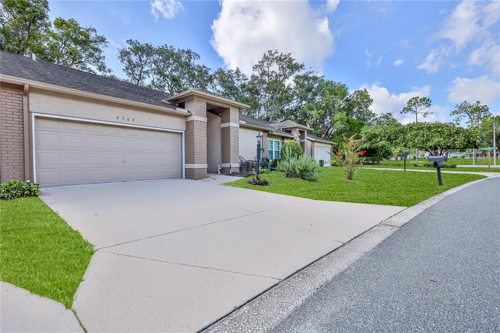 A single-story house with a beige brick facade, a two-car garage, and a concrete driveway — 2468 WHISPERING PINES COURT, SPRING HILL, FL