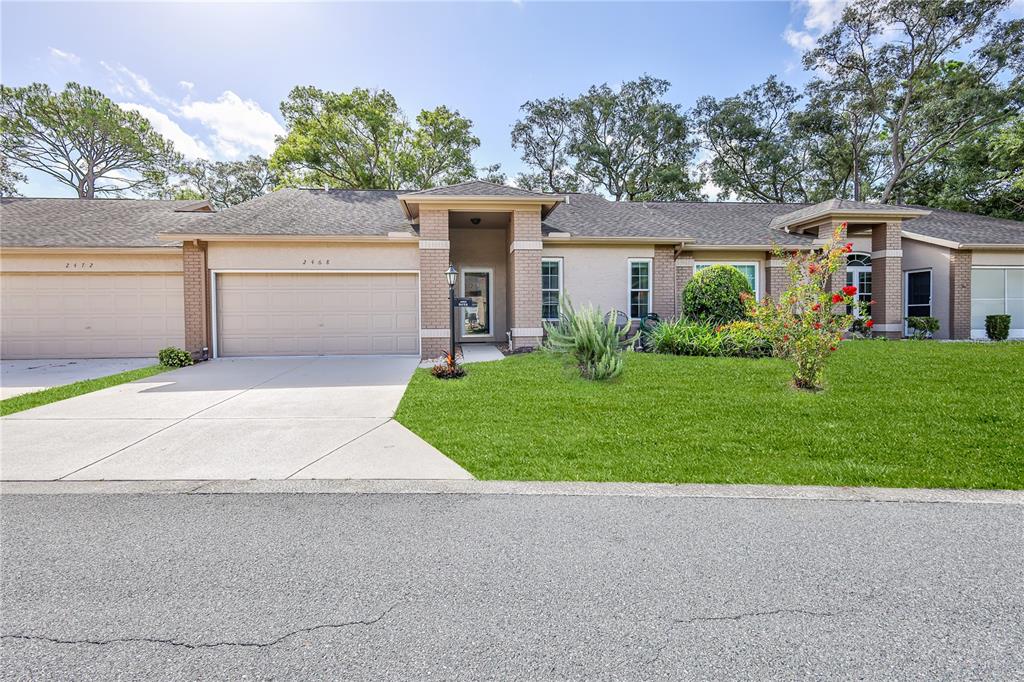 A single-story suburban house with a tan stucco exterior, a two-car garage, and a lawn — 2468 WHISPERING PINES COURT, SPRING HILL, FL