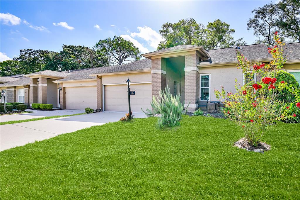 A single-story suburban house with a tan stucco exterior, brick accents, and a two-car garage — 2468 WHISPERING PINES COURT, SPRING HILL, FL