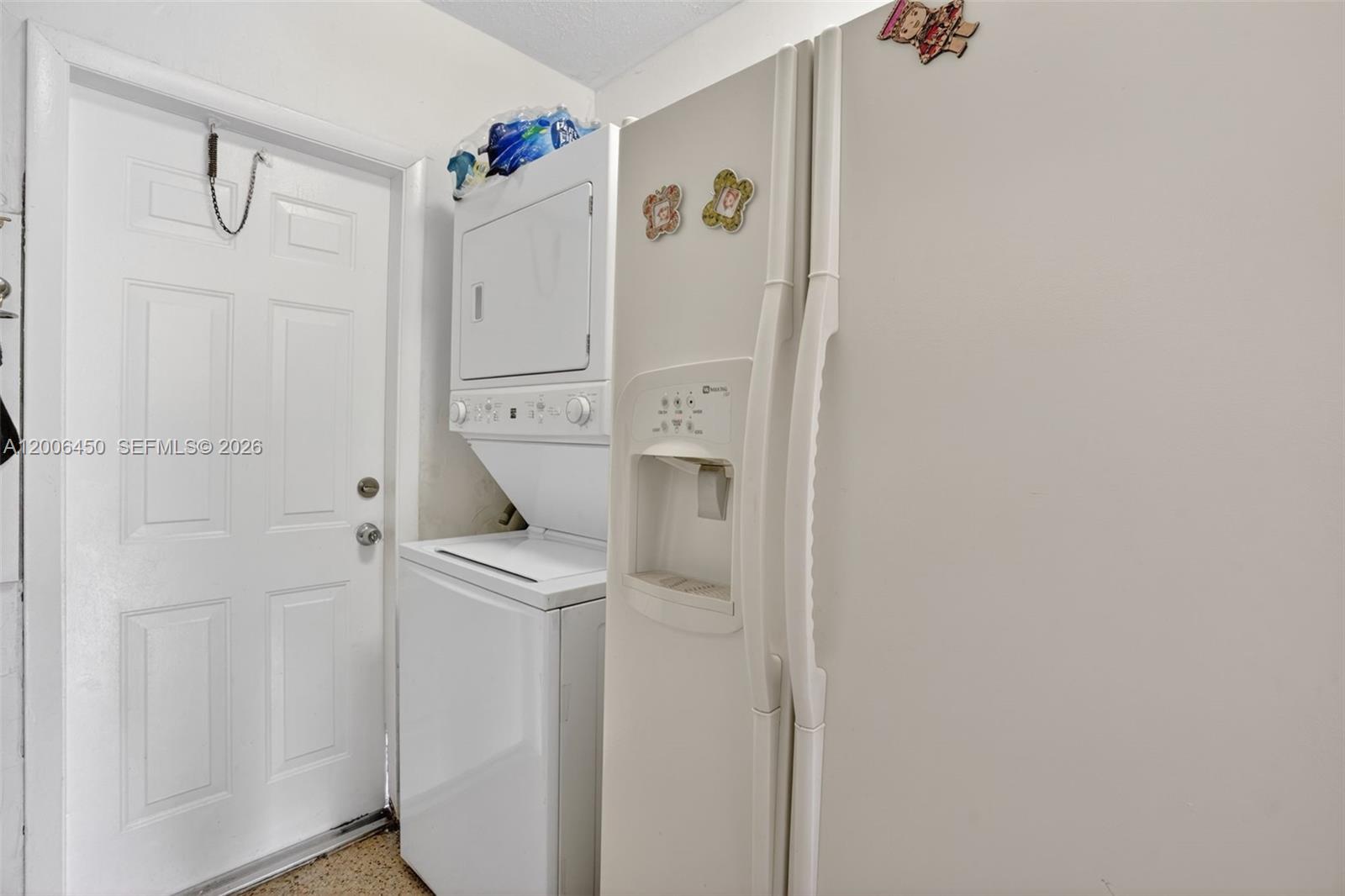A white refrigerator and a stacked washer and dryer unit sit next to a door — 2100 NW 24th St, Miami FL 33142, MIAMI, FL