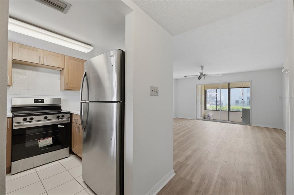 A kitchen with stainless steel appliances and light wood cabinets opens into a living area — 5207 TURQUOISE LANE UNIT 101, NEW PORT RICHEY, FL