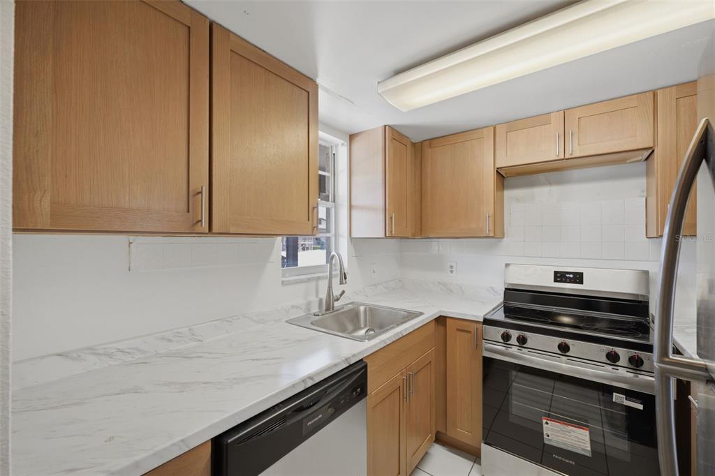 A kitchen features light wood cabinets, white marble-patterned countertops, and stainless steel appliances — 5207 TURQUOISE LANE UNIT 101, NEW PORT RICHEY, FL