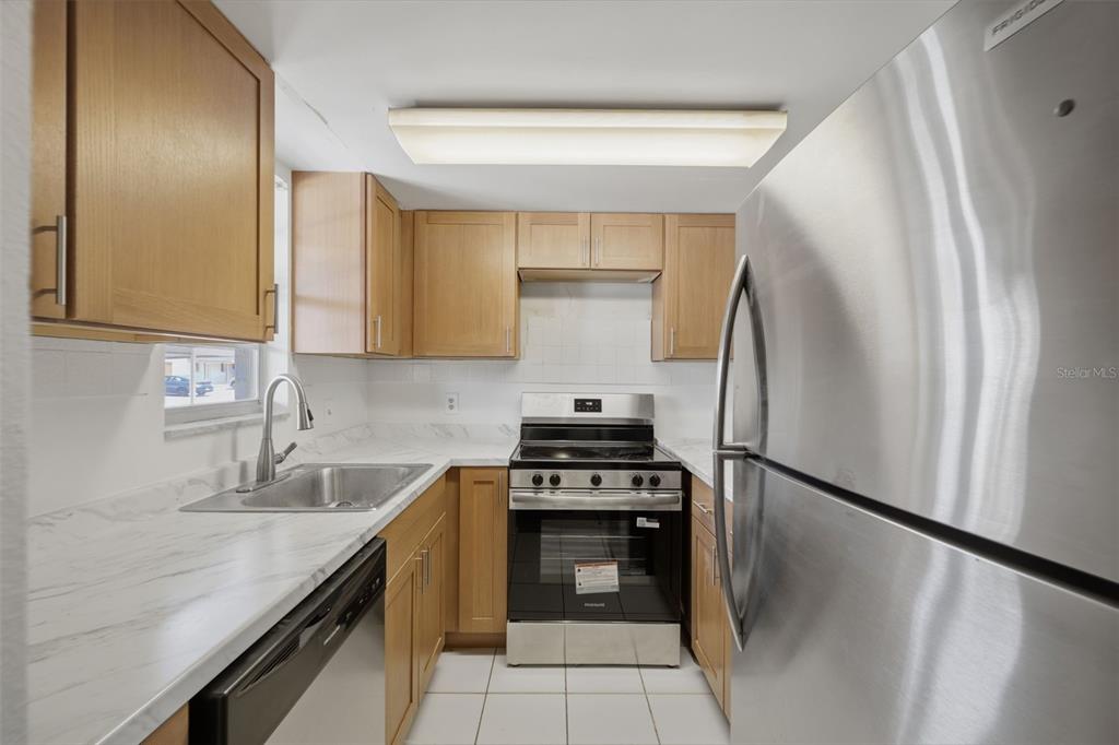 A kitchen features light wood cabinets, white marble-look countertops, stainless steel appliances, and tile flooring — 5207 TURQUOISE LANE UNIT 101, NEW PORT RICHEY, FL