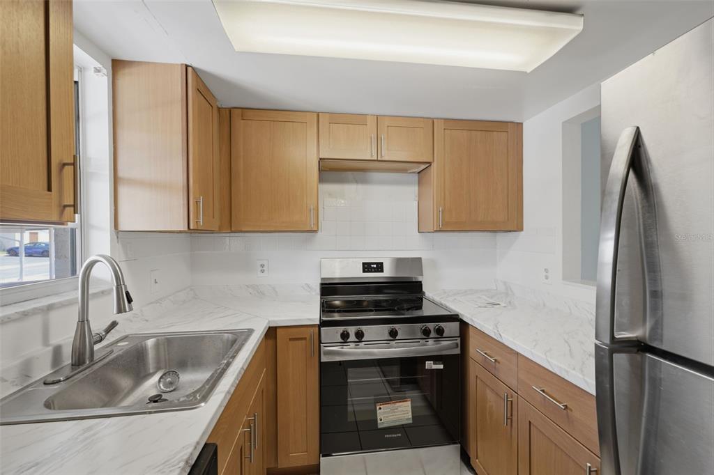 A kitchen features light wood cabinets, white marble-patterned countertops, and stainless steel appliances — 5207 TURQUOISE LANE UNIT 101, NEW PORT RICHEY, FL
