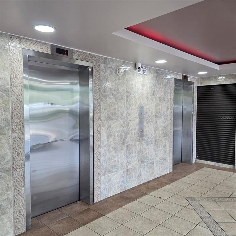 Two stainless steel elevators are set into a tiled wall in a building lobby — 424 CALLE ENSENADA UNIT 307, SAN JUAN, PR