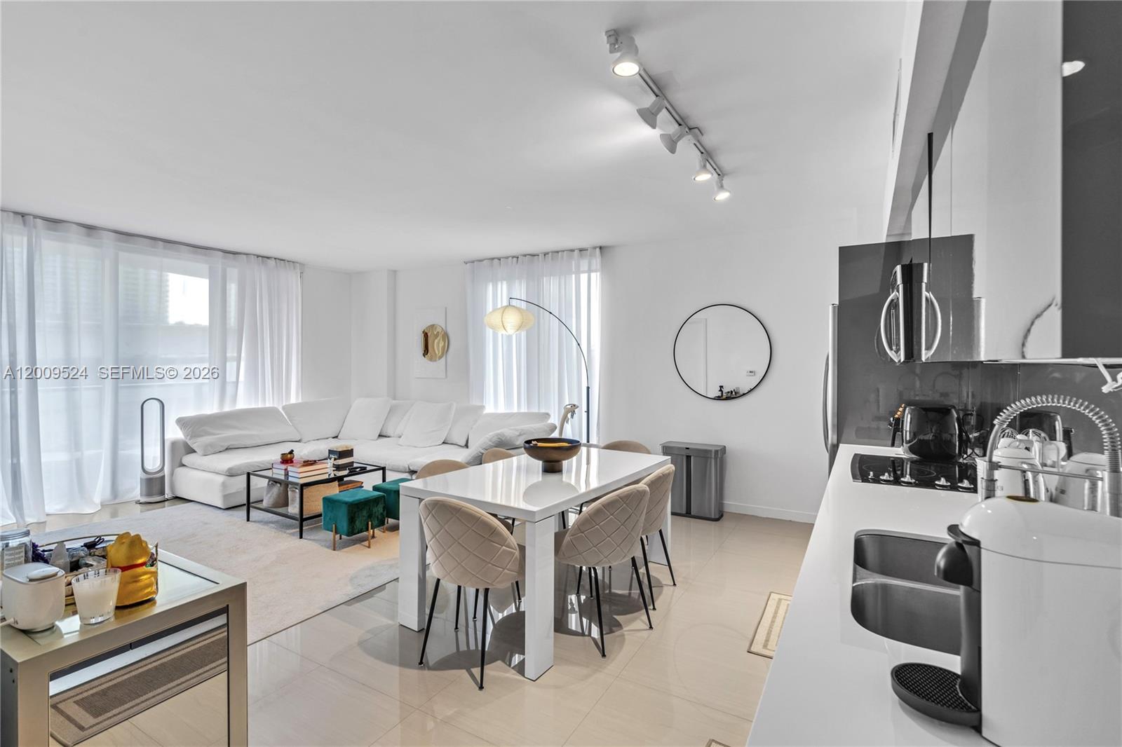 A modern open-concept living and dining area features white furniture, tile floors, and track lighting — 31 SE 6th St # 702, Miami FL 33131, MIAMI, FL