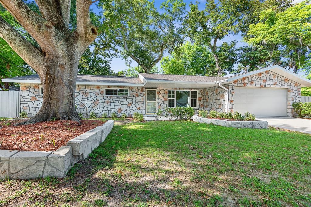 A single-story house with a stone facade, a two-car garage, and a large front tree — 107 WIMBLEDON COURT, PORT ORANGE, FL