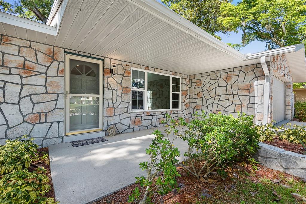 A stone-faced house exterior features a covered concrete porch, a front door, and large windows — 107 WIMBLEDON COURT, PORT ORANGE, FL