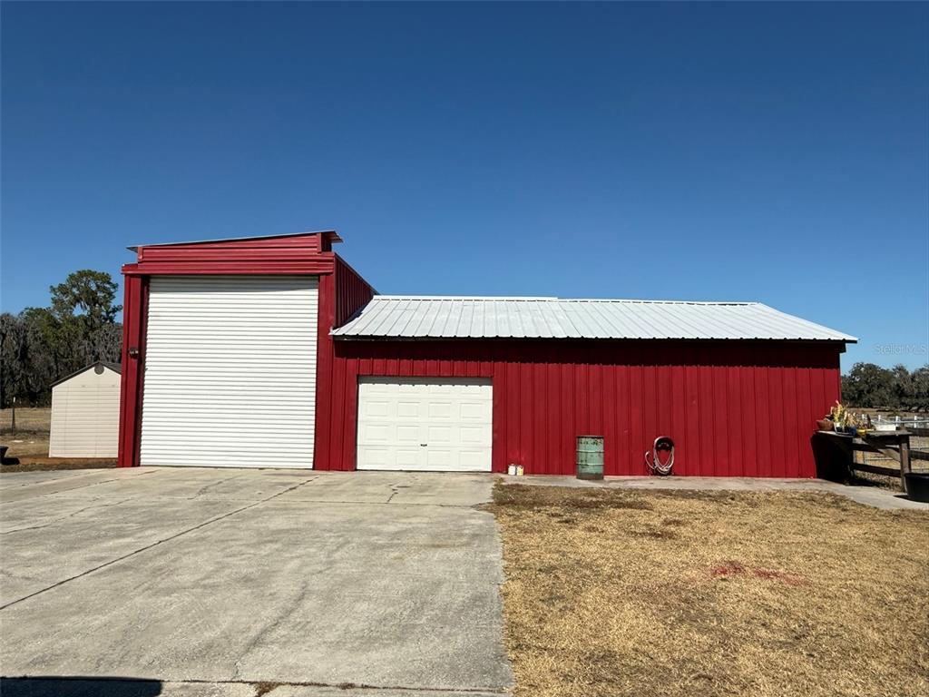 A red metal barn with a tall roll-up door and a standard garage door — 1815 EWELL ROAD, LAKELAND, FL
