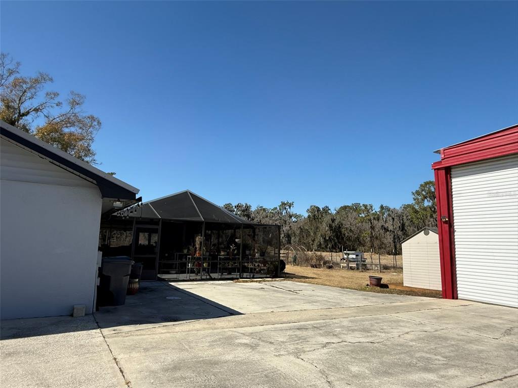 A concrete driveway sits between a house with a screened patio and a metal garage — 1815 EWELL ROAD, LAKELAND, FL