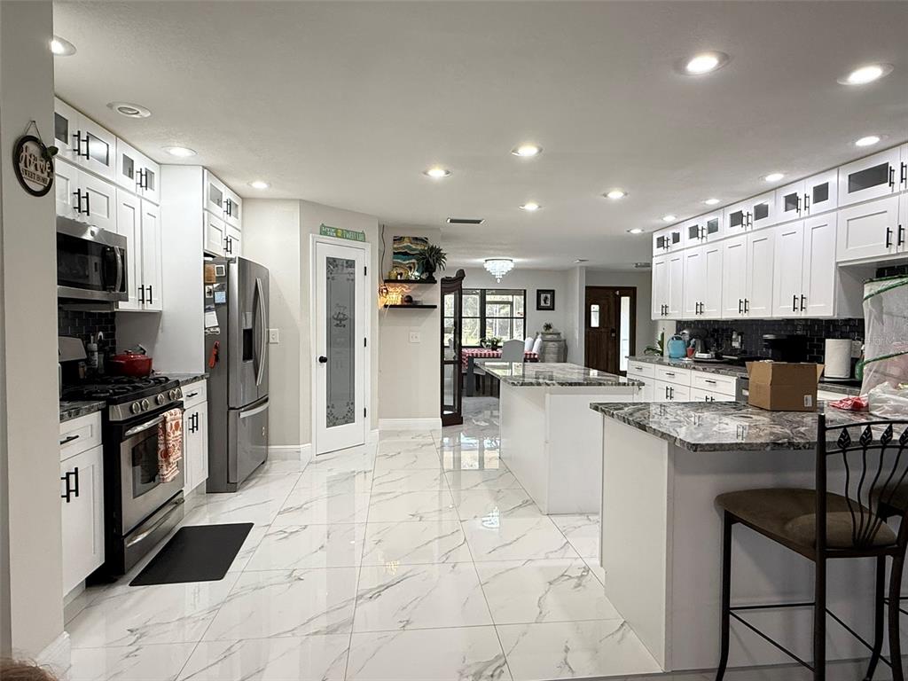 A bright, modern kitchen features white cabinets, marble-patterned tile floors, and a large center island — 1815 EWELL ROAD, LAKELAND, FL