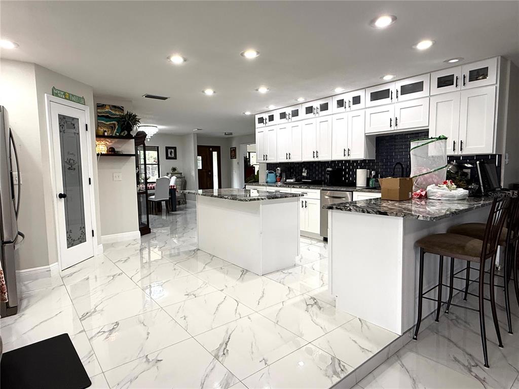 A modern kitchen features white cabinetry, granite countertops, a central island, and white marble flooring — 1815 EWELL ROAD, LAKELAND, FL
