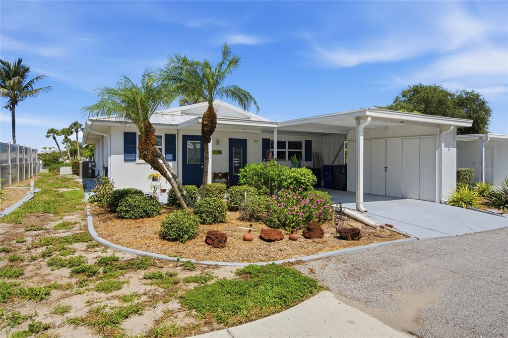 A single-story white house with blue shutters, a carport, and a landscaped front yard — 402 KETCH WAY UNIT 402, NOKOMIS, FL
