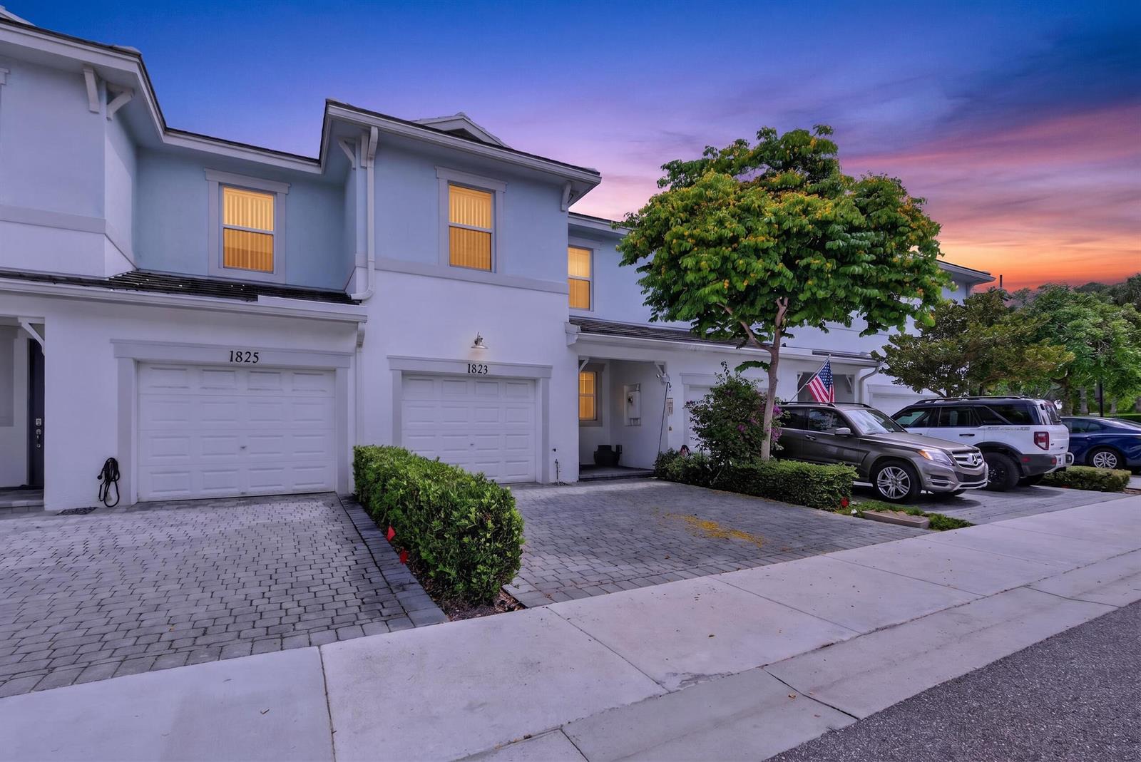 A two-story townhouse exterior with a paved driveway, two garage doors, and a small tree — 1823 Sandpiper Pointe Place, Deerfield Beach FL 33442, DEERFIELD BEACH, FL