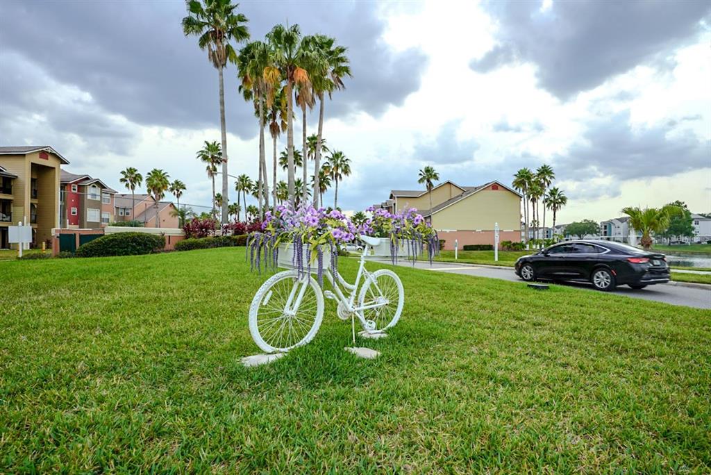 A white decorative bicycle planter sits on a grassy lawn in front of apartment buildings — 2208 ANTIGUA PLACE UNIT 932, KISSIMMEE, FL