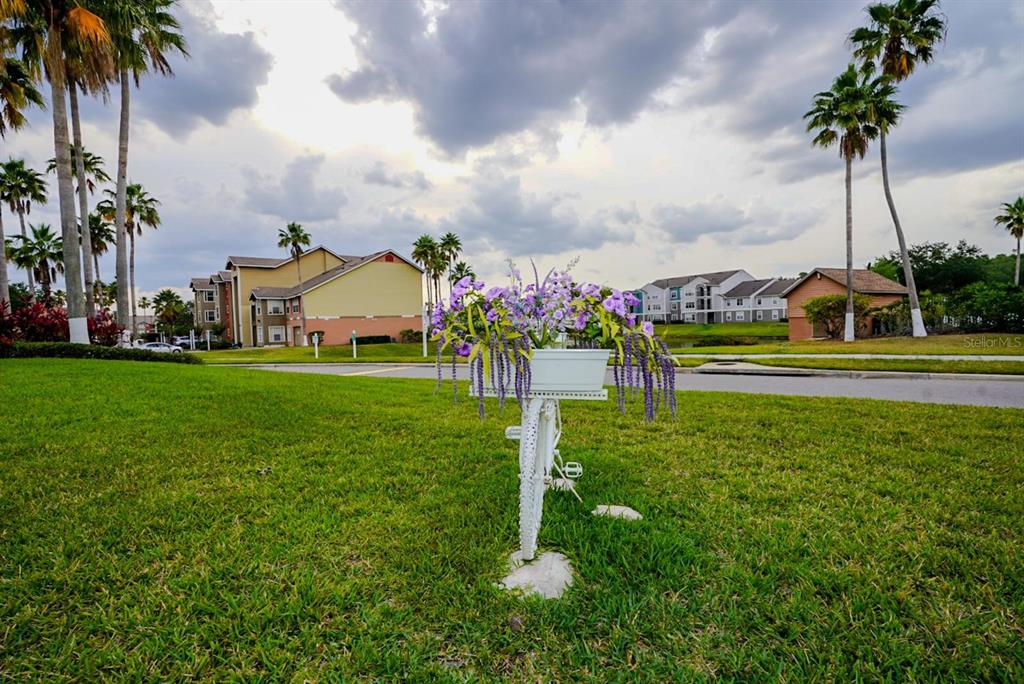 A white decorative bicycle planter filled with purple flowers sits on a grassy lawn — 2208 ANTIGUA PLACE UNIT 932, KISSIMMEE, FL