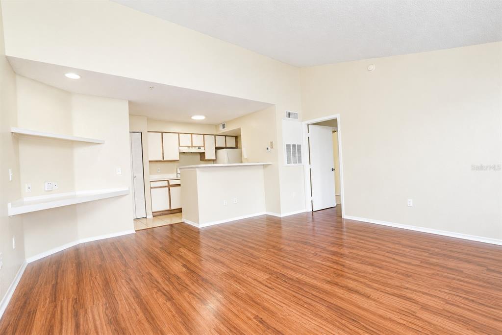 An open-concept living area with wood-look flooring, a kitchen breakfast bar, and built-in shelving — 2208 ANTIGUA PLACE UNIT 932, KISSIMMEE, FL