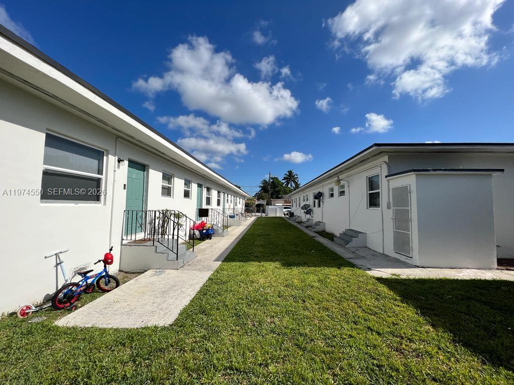 A grassy courtyard sits between two white single-story apartment buildings under a blue sky — 2150 NW 24th St, Miami FL 33142, MIAMI, FL